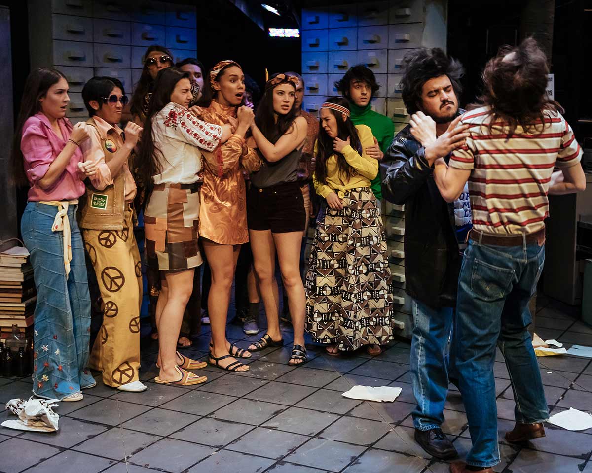 A collection of the actors on stage half way through the show as the colour palette is transitioning from vibrant to sepia through various costumes changes.